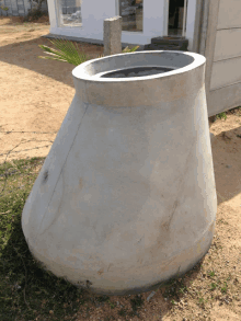 a large concrete cone with a hole in the middle sits in the dirt in front of a building