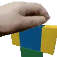 a pixelated image of a person 's hand holding a blue and yellow block .