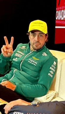 a man wearing a green jacket and a yellow hat giving the peace sign