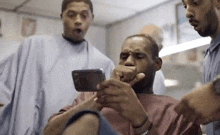 a man is getting his hair cut by a barber while looking at his phone .