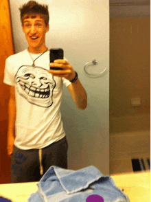 a young man taking a picture of himself in a mirror with a troll face on his shirt