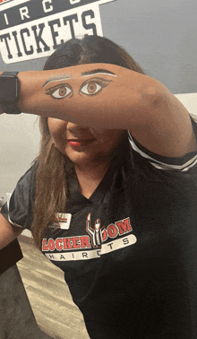 a woman wearing a black locker room haircuts shirt covering her face with her arm