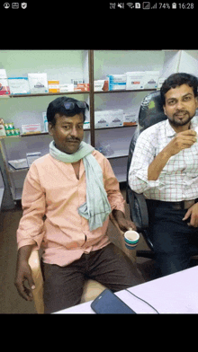 a man in a pink shirt is sitting next to another man drinking from a cup