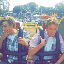 two men are riding a roller coaster at a carnival with a sign in the background that says 020 jju