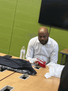 a man in a white shirt sits at a table with a bottle of water on it