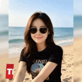 a woman wearing sunglasses and a t-shirt that says ' bana ' on it sits on the beach