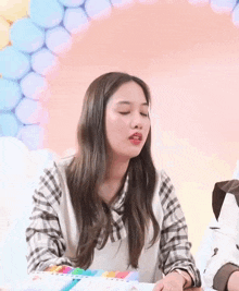a young woman is sitting at a table with balloons in the background and making a funny face .