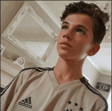 a young boy wearing an adidas shirt is standing in a living room .