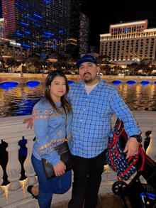 a man and a woman are posing for a photo in front of a body of water