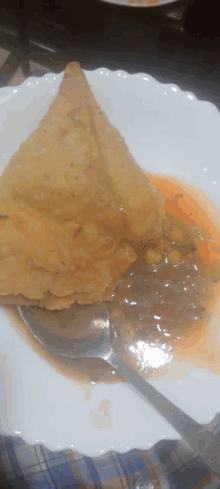 a white plate topped with a triangle shaped fried food and a spoon