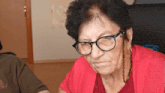 an elderly woman wearing glasses and a red shirt looks at the camera