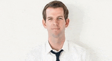 a man in a white shirt and tie is standing against a white wall .