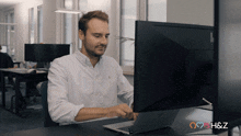 a man sits at a desk with a laptop and a computer monitor with a hearth & z logo on the bottom