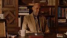 a man sitting at a desk in front of a bookshelf with a mug that says i 'm a scientist