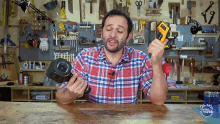 a man in a plaid shirt is holding a dumbbell in front of a workbench with tools on the wall