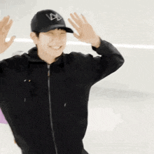 a man wearing a black hat and a black jacket is smiling and waving his hands .