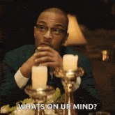 a man in a suit and glasses is sitting at a table with candles and says " whats on ur mind "