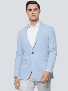 a man is wearing a light blue blazer and white pants