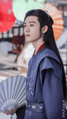 a man with long black hair is holding a fan in front of an umbrella