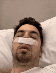 a man laying in a hospital bed with a bandage on his nose