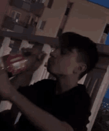 a young man is sitting on a balcony drinking a bottle of soda .