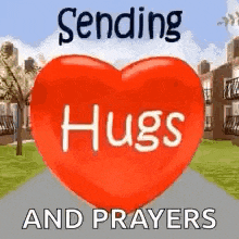 a red heart with the words `` sending hugs and prayers '' written on it is sitting on a sidewalk .