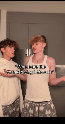 two young men are standing next to each other in a kitchen and one of them says " where are the thanksgiving leftovers " .