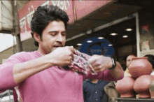 a man in a pink shirt is eating a piece of food in front of a sign that says ' shree '