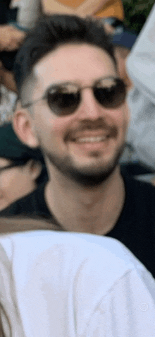 a man with a beard wearing sunglasses is smiling in a crowd