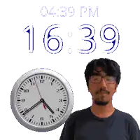 a man wearing glasses stands in front of a clock that says 16:39 pm