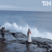 a man is taking a picture of a bride and groom in front of the ocean with the letters th on the bottom