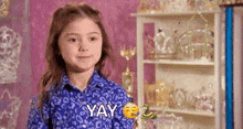 a little girl in a blue shirt is standing in front of a shelf and making a funny face .