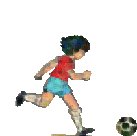 a boy in a red shirt and blue shorts kicking a soccer ball