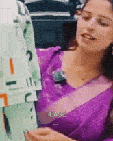 a woman in a purple saree is holding a piece of paper with the word tease written on it