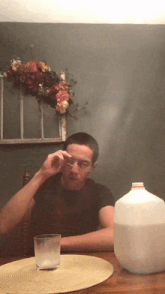 a man wearing glasses sits at a table with a gallon of milk