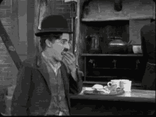 a black and white photo of a man wearing a hat eating a piece of food .