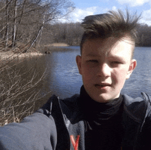 a young boy taking a picture of himself with a lake in the background