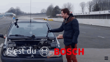 a man stands in front of a car with the hood open and the words c'est du bosch in red