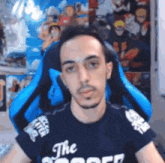 a man is sitting in a blue chair wearing a black t-shirt that says `` the soccer '' .