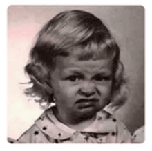 a black and white photo of a little girl with an angry face .
