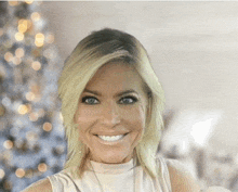 a woman in a white tank top smiles in front of a christmas tree