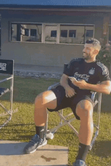 a man in a coca cola shirt sits in a directors chair