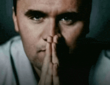 a close up of a man 's face with his hands folded in front of his face