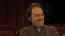 a man is smiling in front of a red curtain that says adult swim on it