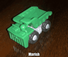 a green toy dump truck sits on a wooden table with the name marish above it