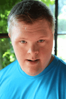 a young man in a blue shirt looks at the camera with his mouth open