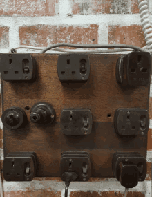 a brick wall with a wooden board with electrical outlets and switches on it