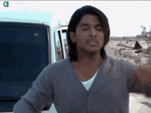a man with long hair is standing in front of a car and making a funny face .
