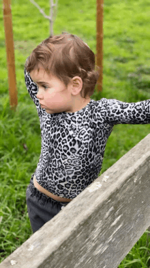 a little girl wearing a leopard print shirt is standing on a wooden railing