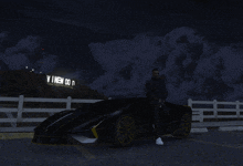 a man stands next to a black sports car in front of a sign that says ' vinen ' on it